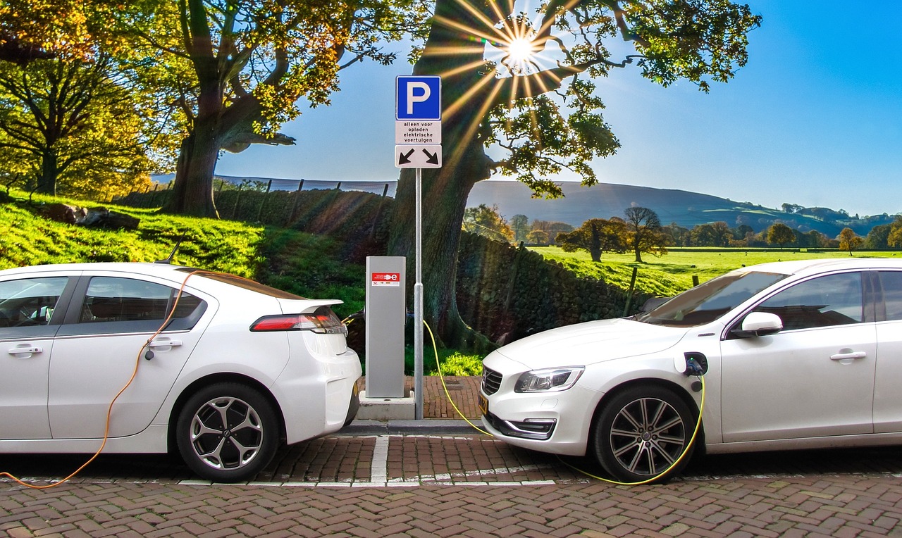 Two white sedans charging at a charging station in front of a beautiful landscape with trees and a field