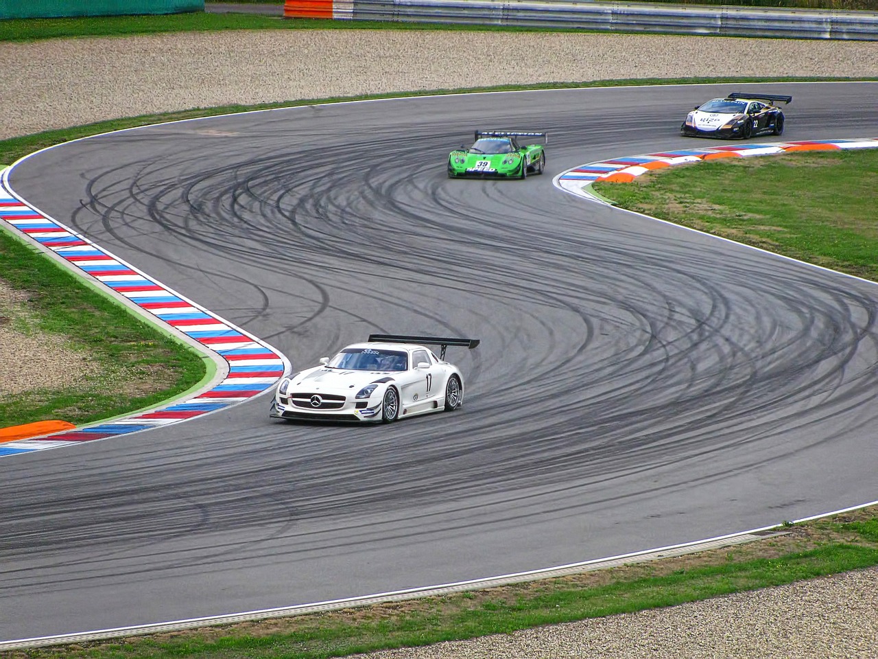 Two white and one green racecar on a serpentine race track.